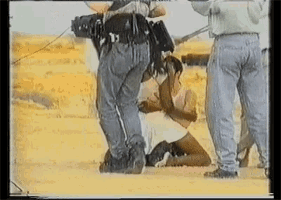 a man in a white shirt is kneeling on the ground while a man in a white shirt stands behind him
