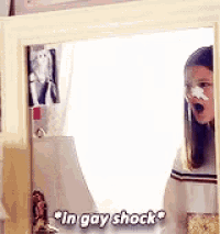 a girl with a bandage on her nose is looking at herself in a mirror and says in gay shock .
