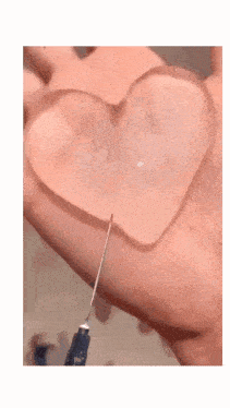 a person is holding a heart shaped object with a syringe in their hand .