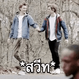 two young men are holding hands while walking down the road .
