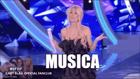 a woman in a black dress stands on a stage holding a microphone and the word musica is on the screen