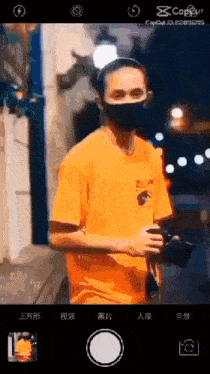 a man wearing an orange shirt and a black mask takes a picture of himself