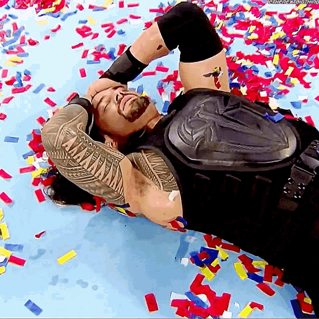 roman reigns is laying on the floor with confetti around him