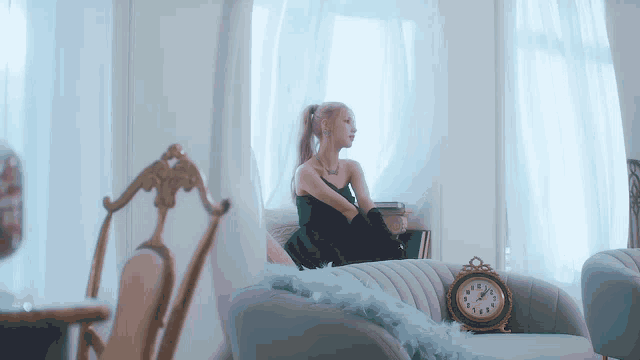 a woman in a black dress sits on a couch next to a clock which shows the time as 4:20