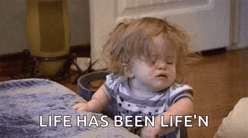 a baby girl is sitting on a bed with the words `` life has been life 'n '' written on the bottom .