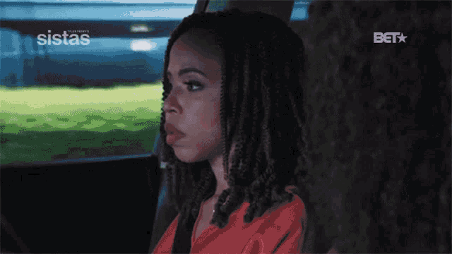 a woman with dreadlocks is sitting in the back seat of a car with bet on the screen