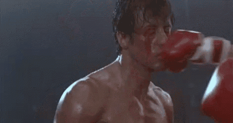 a man in boxing gloves is being hit in the face by another man in a boxing ring .