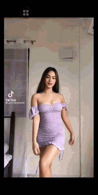a woman in a purple dress is standing in front of a white wall .