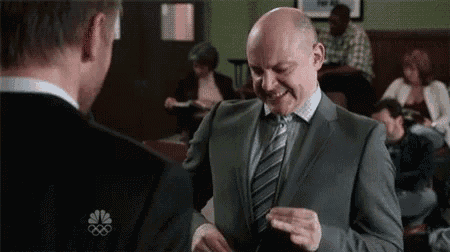 a man in a suit and tie is smiling while talking to another man in a classroom .