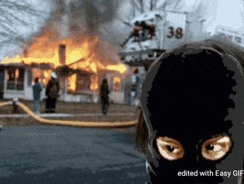 a person wearing a black mask stands in front of a burning house with the number 38 in the background