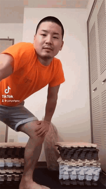 a man wearing an orange shirt and grey shorts stands in front of a wall with a tiktok sticker on it