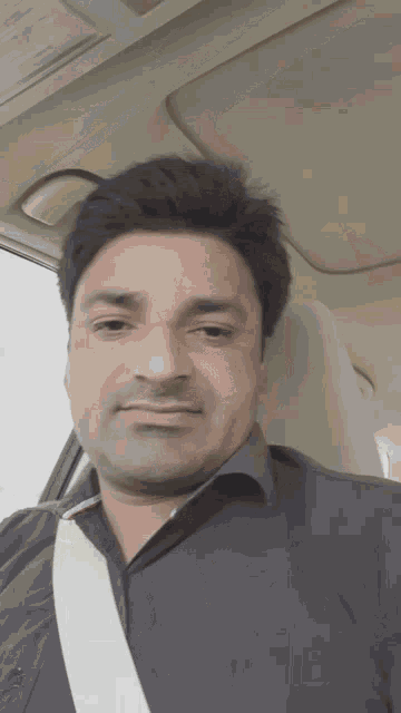 a man wearing a black shirt and a white seat belt looks at the camera