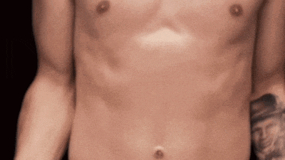 a shirtless man with a tattoo on his arm is standing in a dark room .