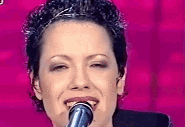 a close up of a woman singing into a microphone on a pink background .