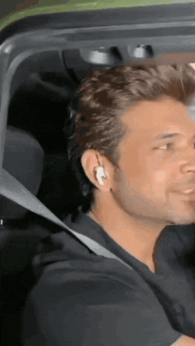 a man wearing a black shirt and white ear buds is sitting in a car