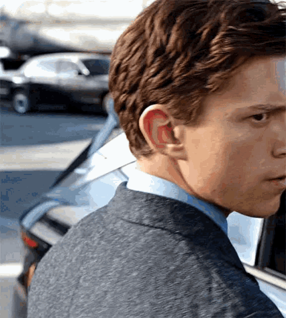 a close up of a man in a suit and blue shirt standing next to a car .