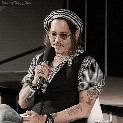 a man wearing a hat and sunglasses is holding a microphone and talking into it .