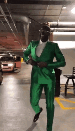 a man in a green suit and hat is dancing in a parking garage .