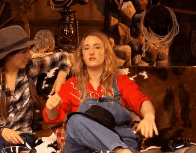 a woman in overalls and a hat sits next to another woman