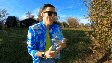 a man in a blue tie dye jacket holds a bottle of water