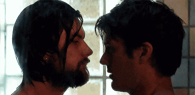 a man with a beard looks at another man 's face