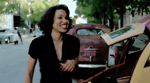 a woman in a black shirt is smiling in front of a car with a license plate that says mtp