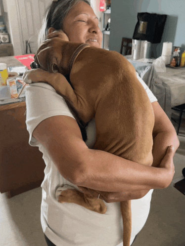 a woman holds a brown dog in her arms