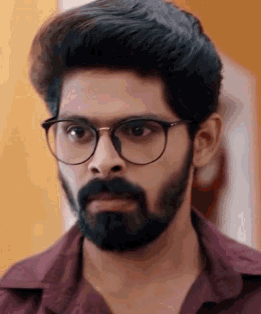 a man with a beard wearing glasses and a purple shirt .