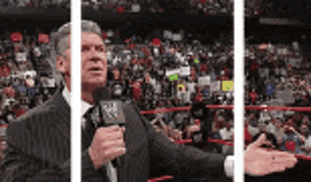a man in a suit and tie is talking into a microphone in front of a crowd .