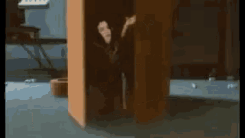 a man is standing in a room behind a wooden pillar .