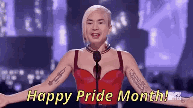 a woman is standing in front of a microphone with her arms outstretched and says `` happy pride month '' .