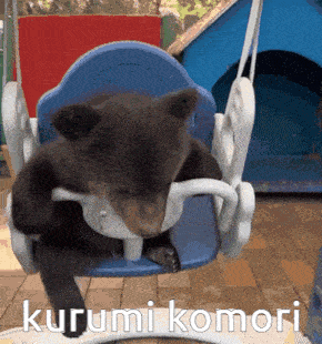 a brown bear is sitting on a blue swing with the words kurumi komori written on the bottom