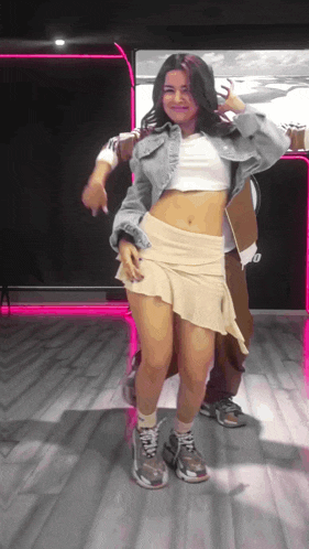 a woman in a crop top and short skirt is dancing with a man in a denim jacket