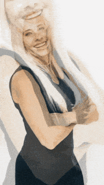a woman with blonde hair and a black tank top smiles with her arms crossed