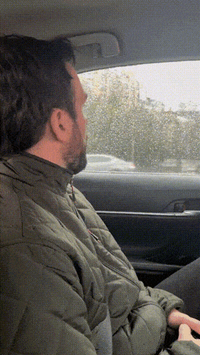 a man in a green jacket sits in a car