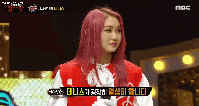 a woman with pink hair is on a stage with a mbc logo behind her
