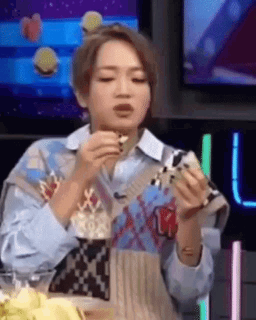 a woman is eating a sandwich while sitting at a table in front of a television .