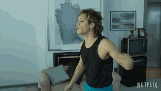 a man in a black tank top is dancing in a living room with a netflix logo behind him