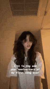 a woman is standing in a hallway and says 2/22 is the one year anniversary of her first song ever