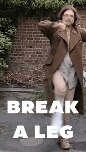 a man in a trench coat is dancing in front of a brick wall with the words break a leg written below him