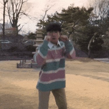 a man wearing a striped shirt is standing in a park
