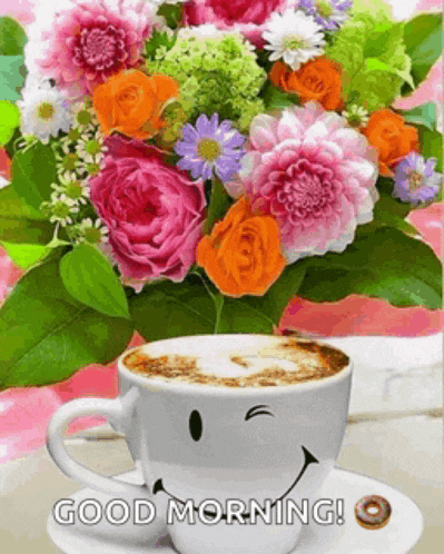 a cup of coffee with a smiley face on it next to a vase of flowers