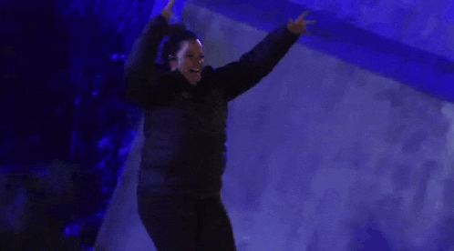 a man in a black jacket is dancing in a dark room with blue lights .