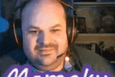 a bald man with a beard wearing headphones and a microphone is sitting in front of a purple sign .