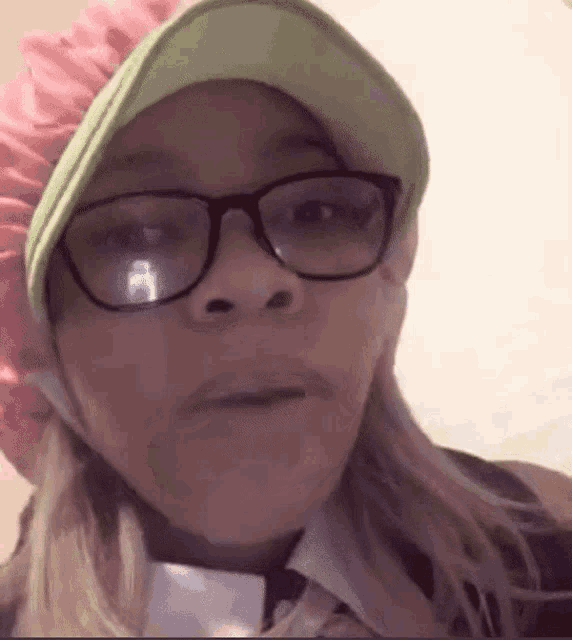 a woman wearing glasses , a pink hat and a green hat is making a funny face .