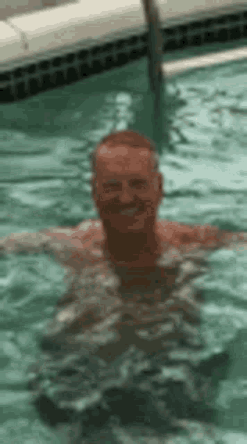 a man is swimming in a pool with his arms outstretched and smiling .