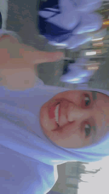 a girl wearing a white hijab is smiling and pointing at the camera .