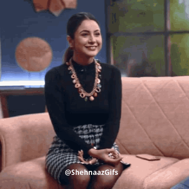 a woman is sitting on a couch wearing a black top and a necklace ..