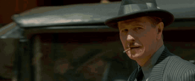 a man in a hat smoking a cigarette in front of a red building