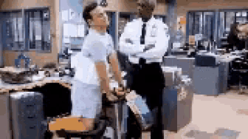 two men are standing in an office talking to each other . one of the men is wearing shorts .